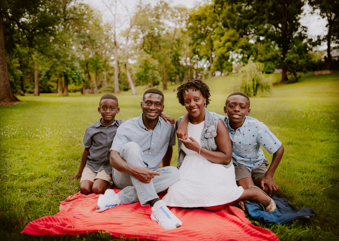 Familie sitzt zusammen auf einer roten Picknickdecke im Park.