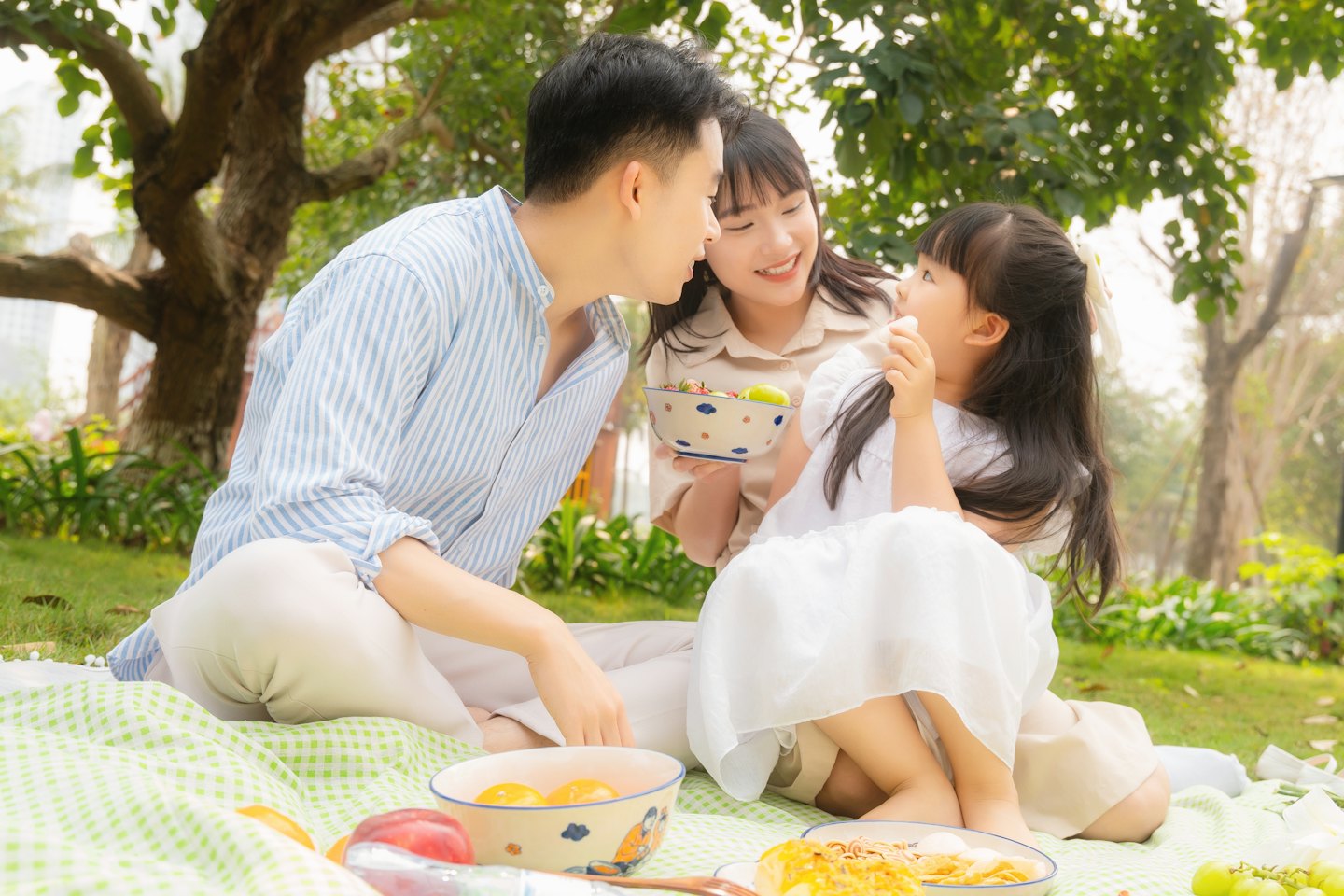 Familie sitzt beim Picknick auf einer karierten Decke im Freien.
